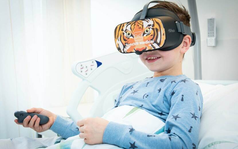 Foto van een glimlachend jong patientje in een ziekenhuisbed met een virtual reality-bril op